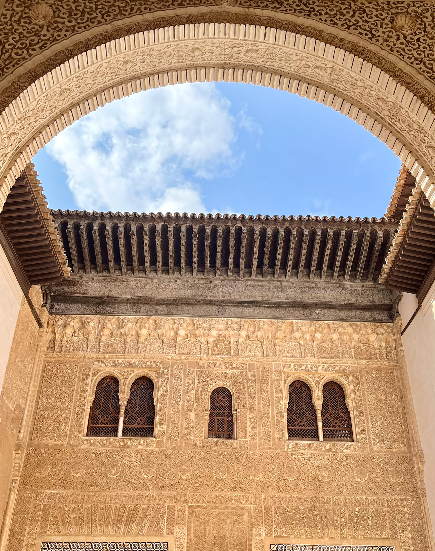 A photo from the inside of the Alhambra. There is an opening in the roof and the sky and clouds peek through the opening.