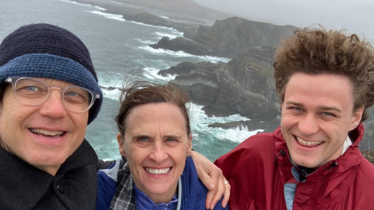 A middle aged man and woman, and a young man pose for a photo at the cliffs of Moher.