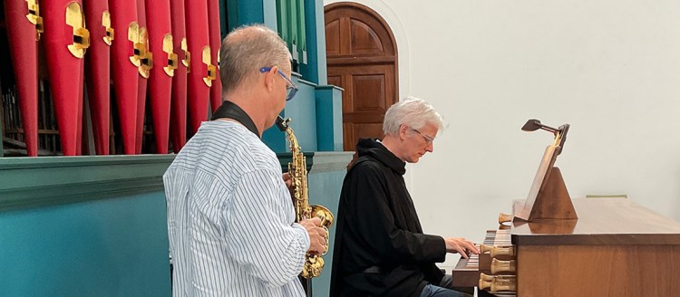 A man plays saxophone while facing a man in black playing the harpsichord.