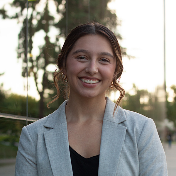 Carli Elisa Medina stands in front of reflective windows trees in the reflection.