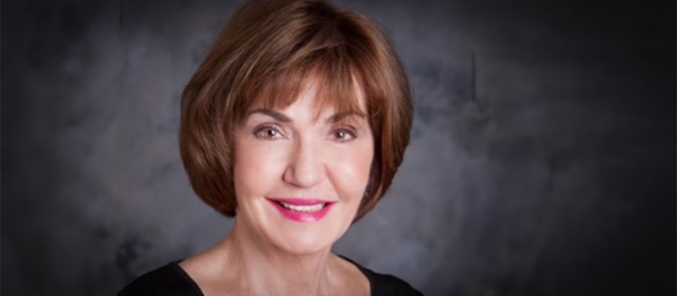 A woman in black poses for a photo. She has brown hair and brown eyes and is looking directly at the camera.