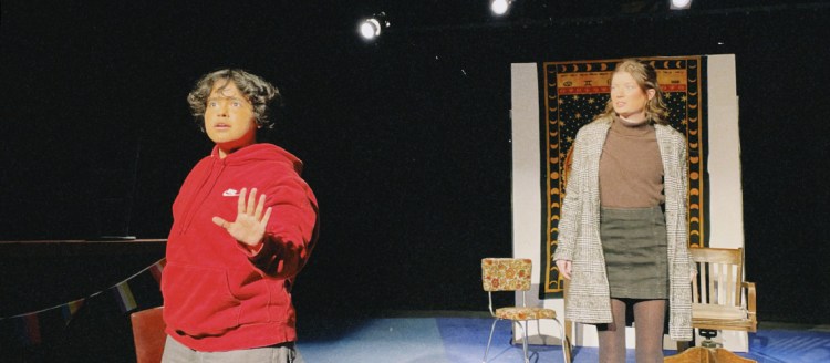 ETC production of "Two Ladies of Vermont" - Two women on stage, one in a red sweatshirt holds up her hand in a "stop" motion. The other in classy earth tone skirt and sweater outfit looks from behind.