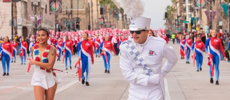 A drum major in white takes a bow with the color guard and band behind him during the 2023 Rose Parade.