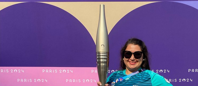 Dr. Tara Hashemi holds the Olympic torch in front of a Paris 2024 backdrop.