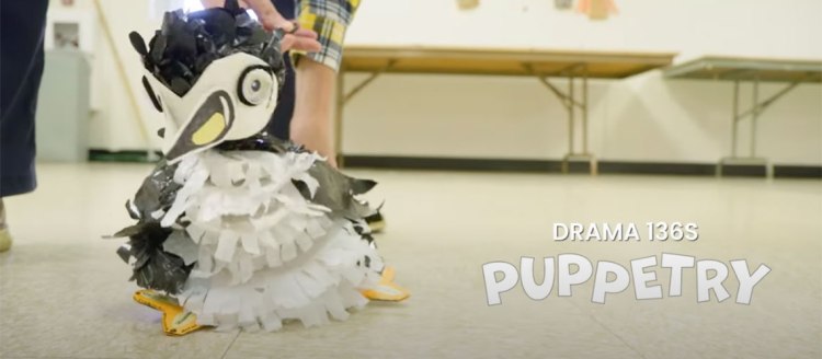A penguin pupper in a classroom. Words read "Drama 136s, Puppetry"