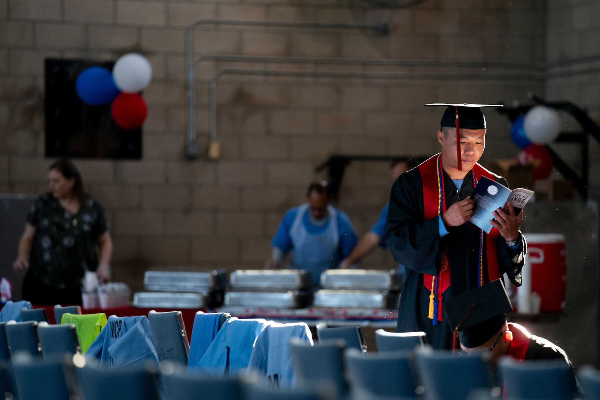 Incarcerated graduate in full regalia reads the commencement program.