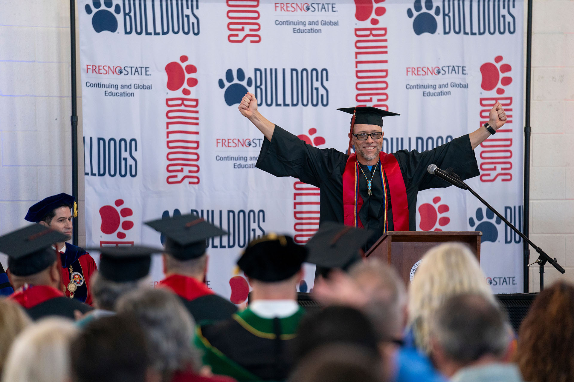 Graduate holds his hands wide with fists clenched in victory during commencement.