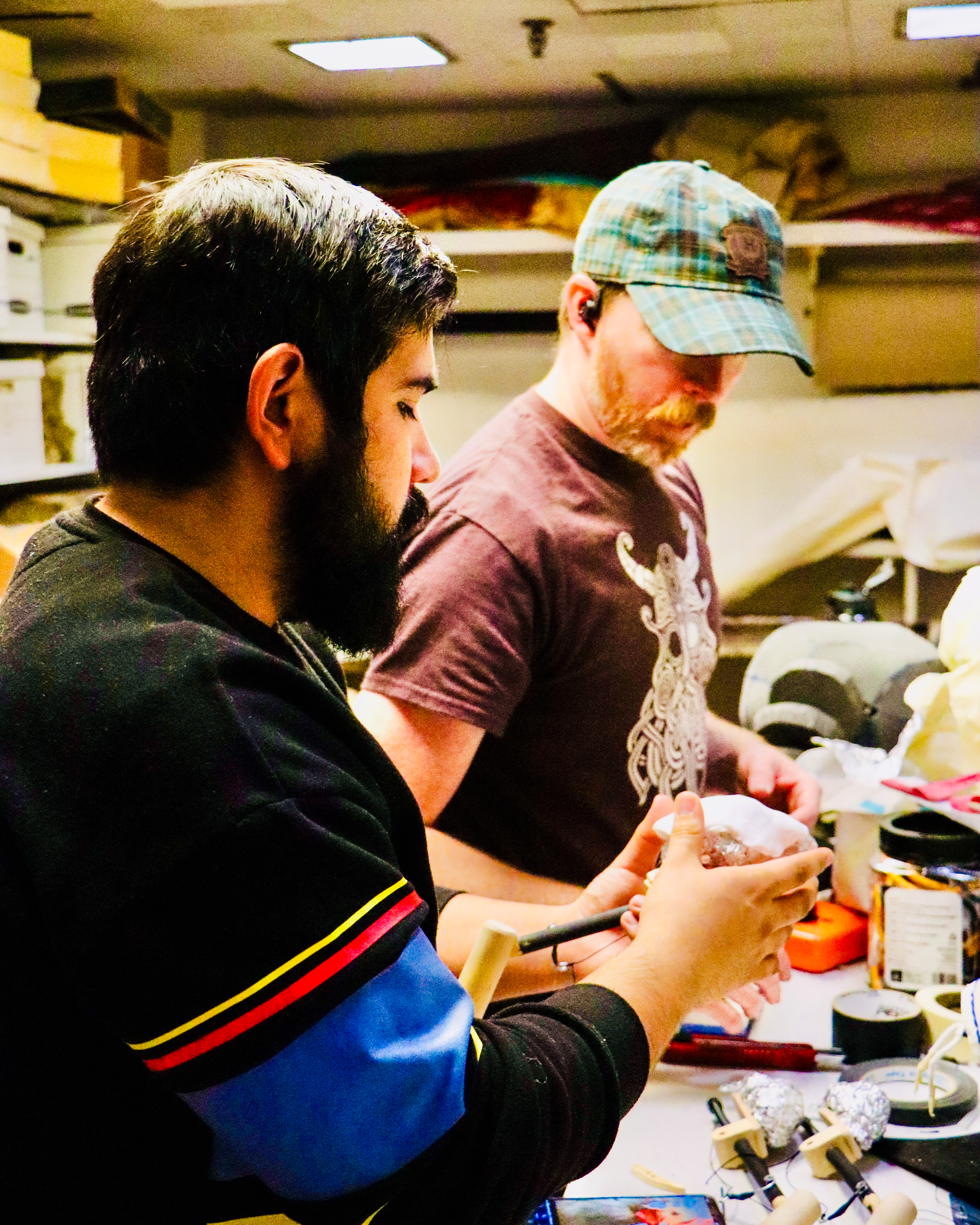 A student and alumnus Matt McGee making puppets at a workbench.