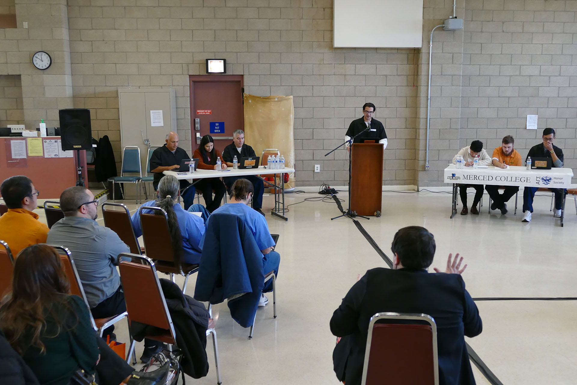 Debate with one student at the podium and others taking notes on each side.