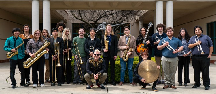 The 2025 Fresno State Jazz Orchestra in front of the music building with their instruments. Director, Richard Giddens squats in the front.