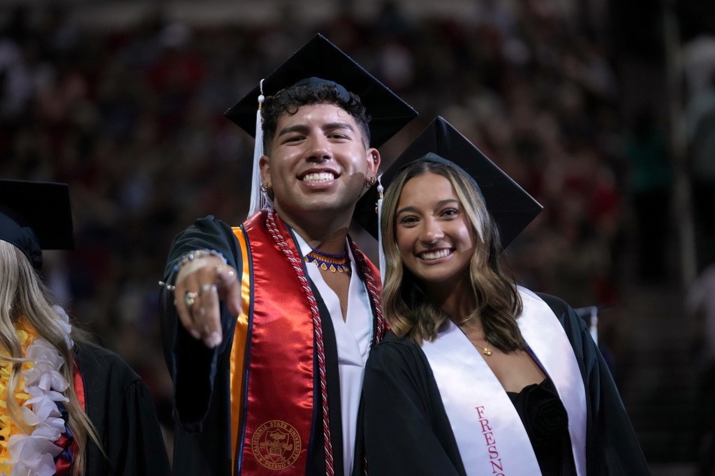 A man and woman grad smile and point for the camera.