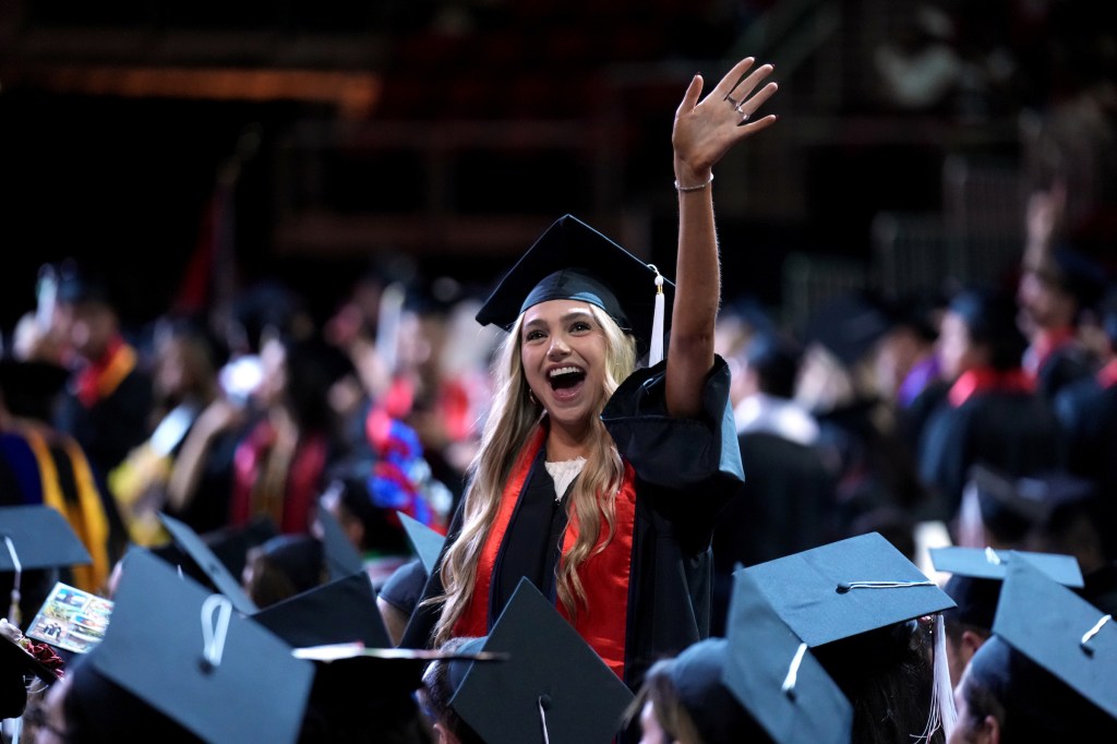 Grad stands and waves amongst sitting grads.