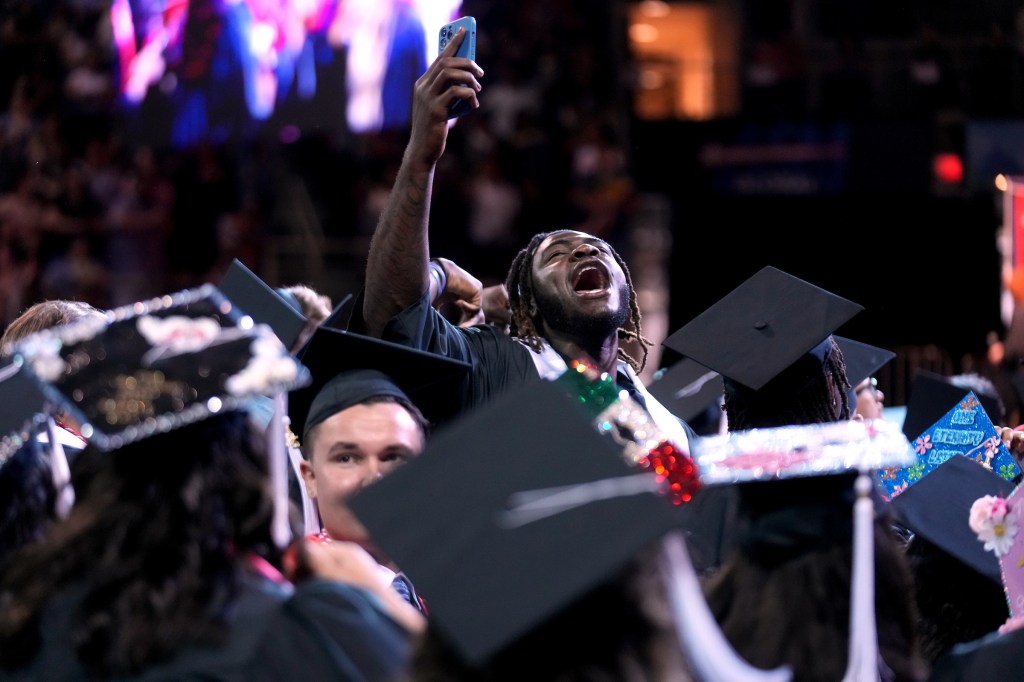 Grad holds up phone while tilting his head up and yelling.