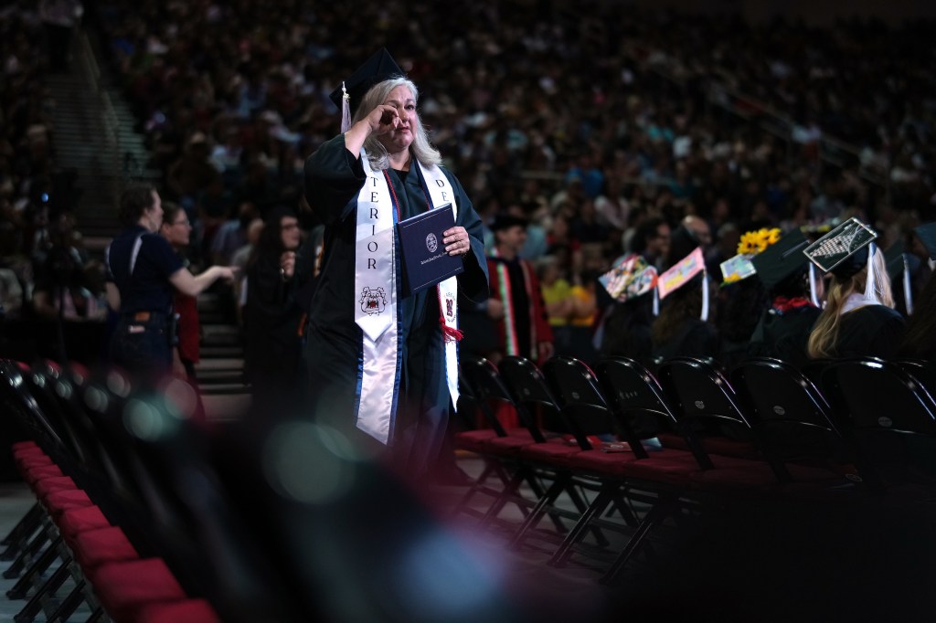 A graduate wipes a tear from her eye as she returns to her seat after walking across the stage.