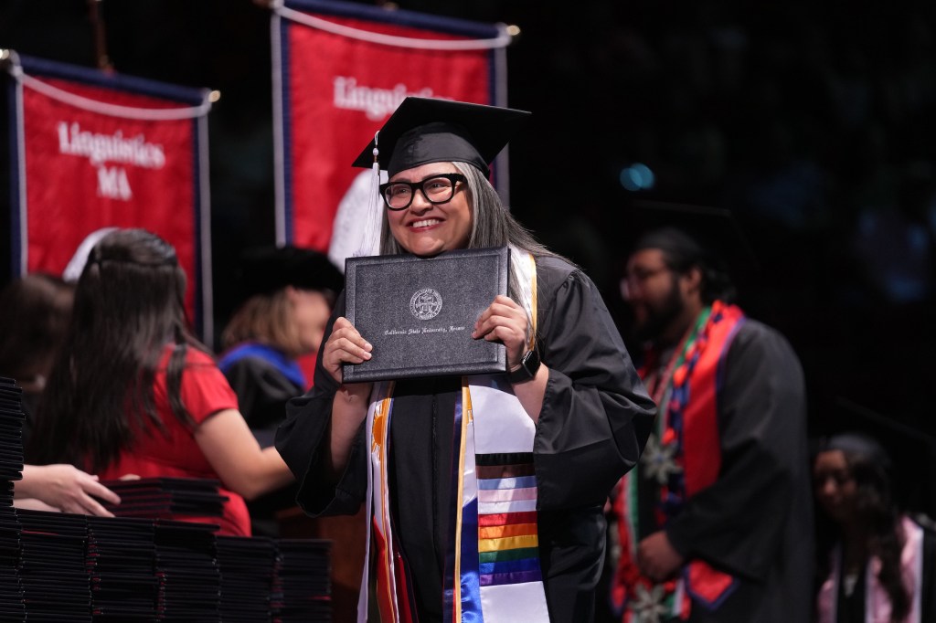 A grad walks across the stage and smiles with her diploma during commencement ceremony.