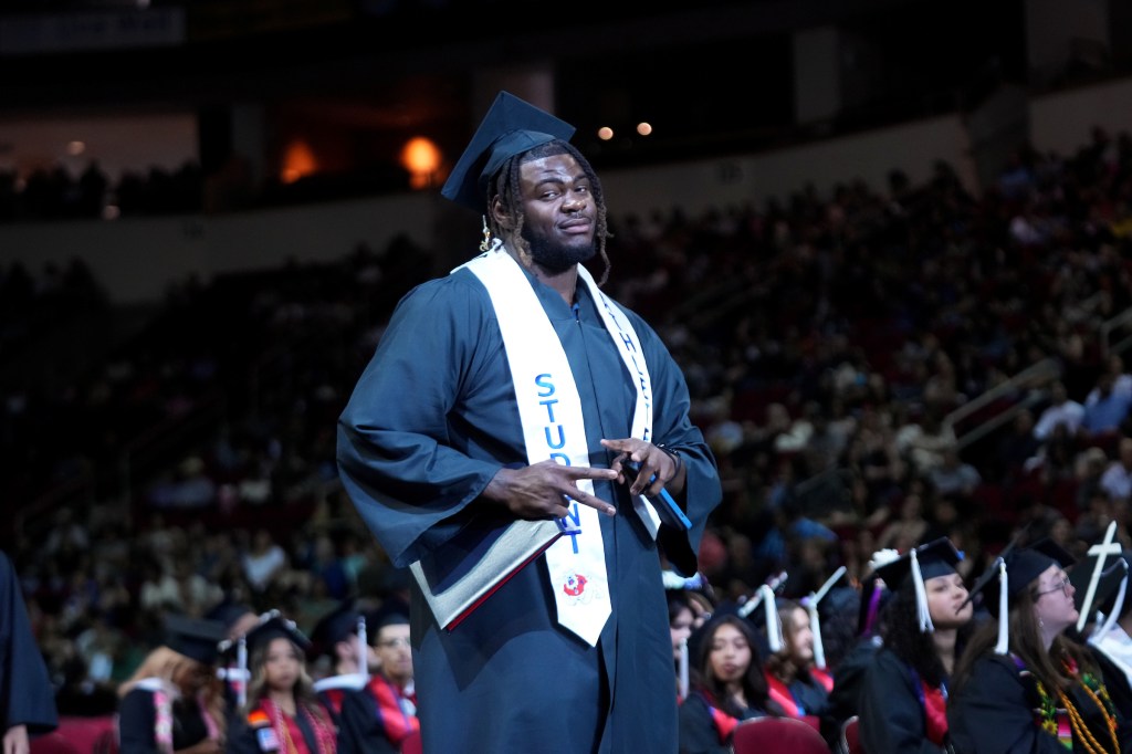 A student athlete grad throws peace signs after walking.