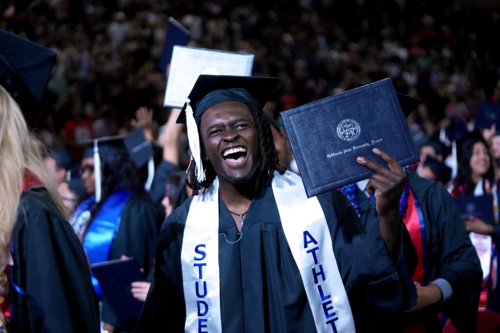 A grad holds up his diploma with a "Student Athlete" stole on.