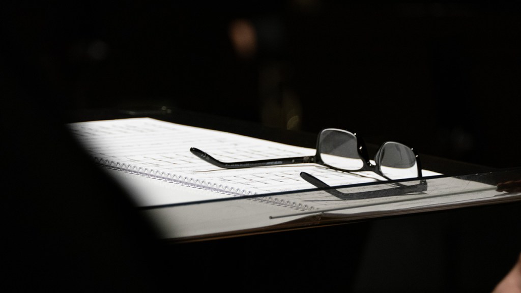A pair of glasses are set on a musical score on the conductor's podium.