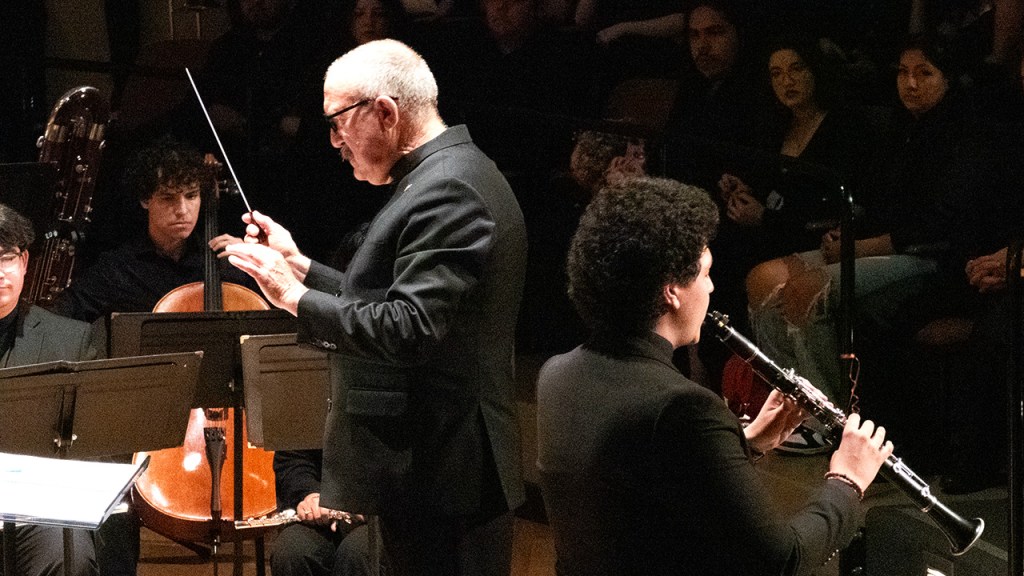 Dr. Gary Gilroy directs the orchestra while a clarinet plays a solo.