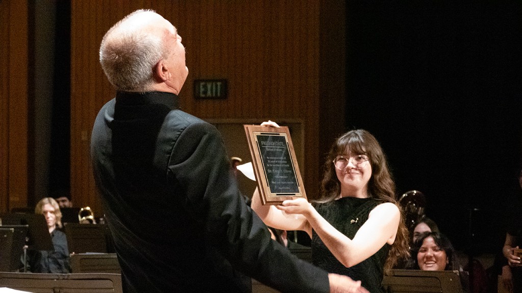 A female student presents a plaque to Dr. Gary Gilroy who is leaning back with laughter.